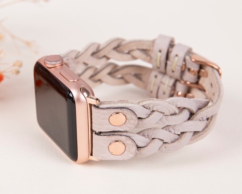 Peut inclure: Une Apple Watch en or rose avec un bracelet en cuir tress&eacute; gris clair. Le bracelet est compos&eacute; de deux rang&eacute;es de tresses et pr&eacute;sente des accents en or rose.