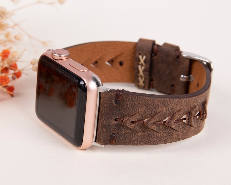 Puede incluir: Una correa de reloj Apple de cuero marr&oacute;n con un dise&ntilde;o trenzado y una hebilla plateada. La correa tiene un aspecto desgastado y est&aacute; hecha de cuero genuino.