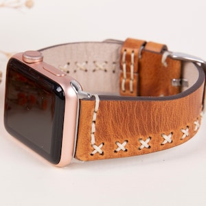 May include: A brown leather Apple Watch band with white stitching. The band has a classic look and is compatible with Apple Watch models.