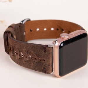 Puede incluir: Una correa de reloj de cuero marr&oacute;n con un dise&ntilde;o trenzado. La correa est&aacute; unida a un Apple Watch de oro rosa.