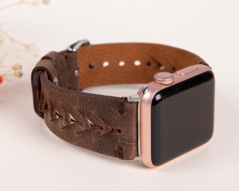 Puede incluir: Una correa de reloj de cuero marr&oacute;n con un dise&ntilde;o trenzado. La correa est&aacute; unida a un Apple Watch de oro rosa.