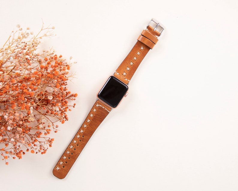 May include: A brown leather watch band with white stitching for an Apple Watch.