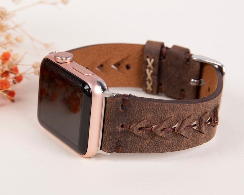 Puede incluir: Una correa de Apple Watch de cuero marr&oacute;n con un dise&ntilde;o trenzado y una hebilla plateada. La correa tiene un aspecto desgastado y est&aacute; hecha de cuero genuino.
