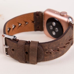 Puede incluir: Una correa de reloj de cuero marr&oacute;n con un dise&ntilde;o trenzado y una hebilla plateada. La correa est&aacute; dise&ntilde;ada para un Apple Watch y tiene una esfera de reloj de oro rosa.