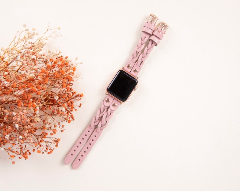Peut inclure: Un bracelet de montre en cuir tress&eacute; rose avec des accents dor&eacute;s et un cadran noir.