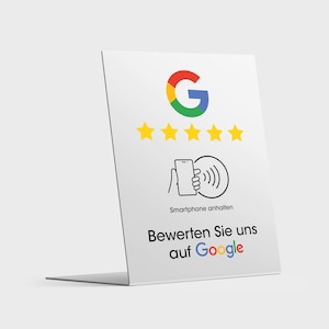 May include: White sign with a Google logo, five yellow stars, and a black and white icon of a hand holding a smartphone near a wavy line. The text on the sign reads "Smartphone anhalten" and "Bewerten Sie uns auf Google".