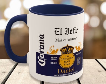 May include: White ceramic mug with a navy blue handle and interior. The mug features the "Corona" logo and the text "El Jefe Mas Chingon" with a crown graphic. The mug also includes the name "Daniel" and "Imported Beer From Mexico".