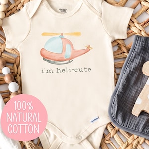 May include: A beige baby onesie with a cartoon helicopter and the text "i'm heli-cute". The onesie is made of 100% natural cotton.