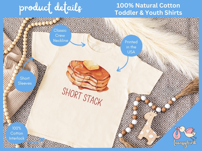 Op de afbeelding: Cr&egrave;mekleurig T-shirt voor peuters en jongeren met een ronde hals en korte mouwen. Het shirt heeft een aquarel illustratie van een kleine stapel pannenkoeken met boter en siroop, met de tekst "SHORT STACK". Gedrukt in de VS.