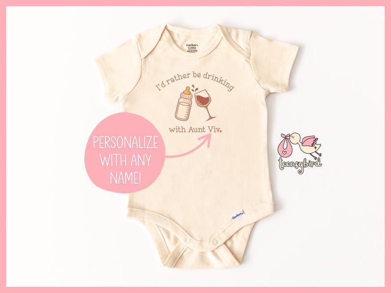 May include: Cream-colored baby onesie with the text "I'd rather be drinking with Aunt Viv." A baby bottle and wine glass are illustrated above the text. A pink circle with the words "Personalize with any name!" is on the left.