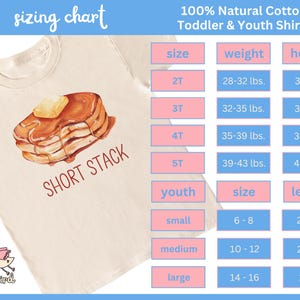 Op de afbeelding: Cr&egrave;mekleurig T-shirt voor peuters en jongeren met een aquarel illustratie van een stapel pannenkoeken met boter en siroop. De tekst "SHORT STACK" staat eronder. Een maattabel is inbegrepen.