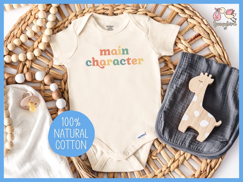 May include: A white baby onesie with the text "main character" in rainbow colors. The onesie is made of 100% natural cotton.