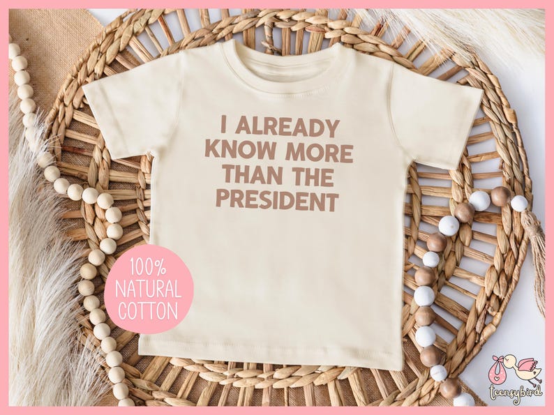 May include: A cream colored baby onesie with the text "I already know more than the president" printed in brown. The onesie is made of 100% natural cotton.