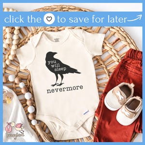May include: A white baby onesie with a black crow illustration and the text "You will sleep nevermore". The onesie is on a woven wicker surface with a wooden bead garland and a pair of red pants and brown shoes.