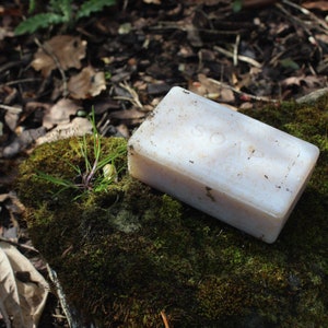 Puede incluir: Una pastilla de jabón blanca con la palabra "SOAP" en relieve, sobre un lecho de musgo verde.
