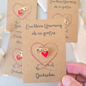 Könnte beinhalten: Mehrere Karten aus Kraftpapier mit einem roten Herzanhänger. Jede Karte hat ein gezeichnetes rotes Herz, den deutschen Text "Eine kleine Umarmung als ein großes" und "Dankeschön".