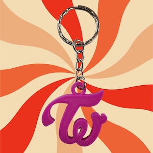 May include: A pink keychain with the stylised letter "T" hanging from a silver chain and ring.