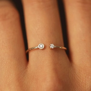 Puede incluir: Un delicado anillo de oro con dos pequeños diamantes, uno a cada lado de la banda.