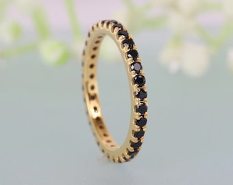 May include: A gold band ring with a row of black gemstones. The ring is set against a light blue background.