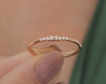 May include: A delicate gold band ring with a row of small diamonds, including a larger rectangular diamond in the center.