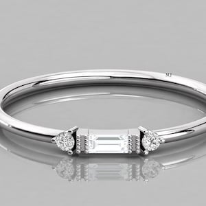 May include: A delicate silver ring featuring a rectangular centre stone and two smaller pear-shaped stones on either side. The ring is set against a white background.