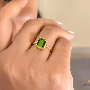 Może przedstawiać: Złoty pierścionek z zielonym kamieniem szlachetnym. Pierścionek jest na palcu.