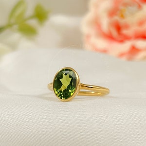Peut inclure: Une bague en or avec une pierre ovale verte. La bague est sur un fond blanc.