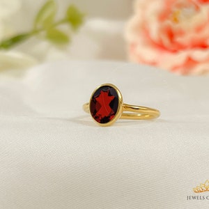 Könnte beinhalten: Ein goldener Ring mit einem roten Edelstein. Der Ring liegt auf einem weißen Stoffhintergrund.