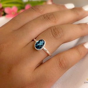 May include: A silver ring with a blue oval gemstone. The ring is on a person's finger.