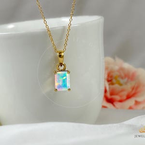 Puede incluir: Un collar de cadena de oro con un colgante que presenta una piedra preciosa de ópalo iridiscente rectangular.