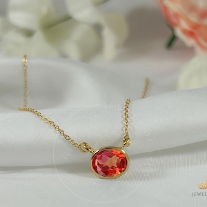 May include: A gold chain necklace with a red gemstone pendant. The pendant is a round, faceted stone with a slightly oval shape.
