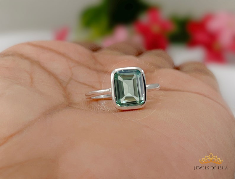 May include: A silver ring with a green emerald-cut gemstone. The ring is on a person's hand.