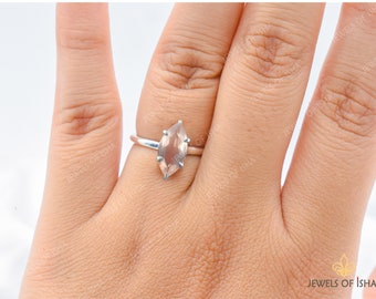 May include: A silver ring with a light brown marquise-shaped gemstone. The ring is on a person's finger.