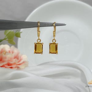 Puede incluir: Un par de pendientes de oro con una piedra preciosa de ámbar cuadrada. Los pendientes cuelgan de un simple gancho de oro.