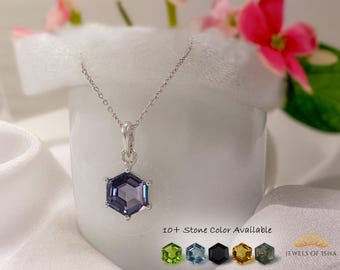 Puede incluir: Un collar de plata con un colgante de piedra preciosa hexagonal de color púrpura sujeto por seis garras. El texto 10+ Stone Color Available aparece junto a cinco iconos de piedras hexagonales y el texto JEWELS OF ISHA.
