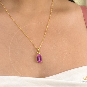 May include: A gold chain necklace with a pendant featuring a faceted, purple gemstone. The pendant is shaped like a long, narrow hexagon.