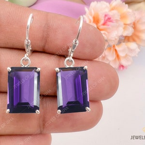 May include: A pair of silver dangle earrings featuring rectangular purple amethyst gemstones. The earrings have a simple design and are ideal for everyday wear.