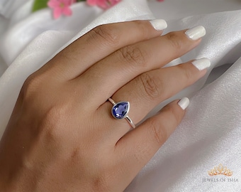 May include: A silver ring featuring a pear-shaped blue gemstone. The ring is worn on a finger.