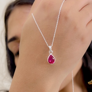 May include: A silver chain necklace with a teardrop-shaped pendant featuring a pink gemstone.