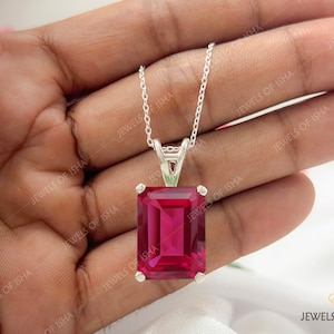 May include: A silver chain necklace with a pendant featuring a large, square-shaped, deep red gemstone.