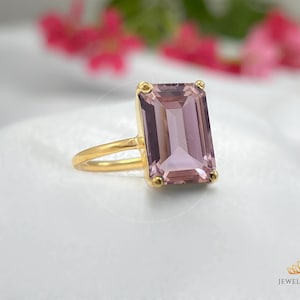 May include: A gold ring featuring a large, rectangular, light purple gemstone. The gemstone is set in a gold bezel setting.