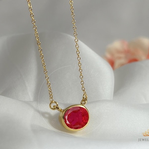 Puede incluir: Un collar de cadena dorada con un colgante de piedra ovalada roja.