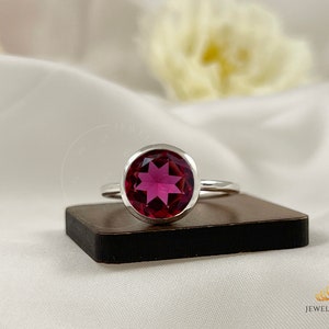 Peut inclure: Une bague en argent avec une grande pierre précieuse ronde, facetée et rose. La pierre précieuse a un motif en forme d'étoile à l'intérieur.