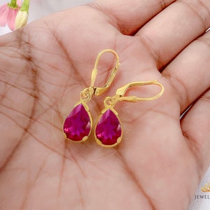 May include: A pair of gold dangle earrings with teardrop-shaped pink gemstones.