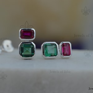 May include: A pair of silver earrings featuring a vertical arrangement of a rectangular magenta gemstone and a square green gemstone, alongside a second pair of earrings with a square green gemstone and a rectangular magenta gemstone.