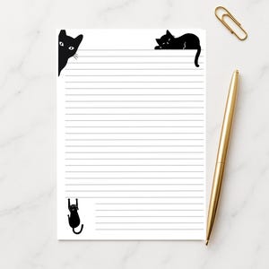 May include: White lined notepad with black cat illustrations. A gold pen and paperclip are on the right. The cats are in various poses, including peeking from the corner, lounging, and hanging.