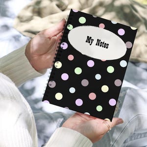 May include: A spiral-bound notebook with a black cover featuring a pattern of multicolored polka dots in shades of pink, yellow, blue, and green. A white oval shape is centered on the front cover with the black text My Notes printed inside.