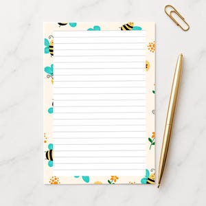 May include: A lined notepad with a cream-colored background and a border of cartoon bees and flowers. A gold pen and paperclip are next to the notepad. The notepad is designed for writing notes.