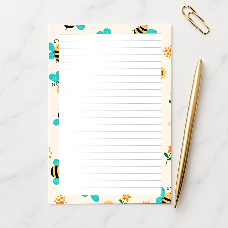 May include: A lined notepad with a cream-colored background and a border of cartoon bees and flowers. A gold pen and paperclip are next to the notepad. The notepad is designed for writing notes.