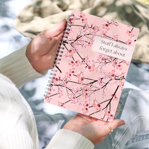 Può includere: Un quaderno rosa con un design floreale e il testo "Stuff I always forget about" sulla copertina.